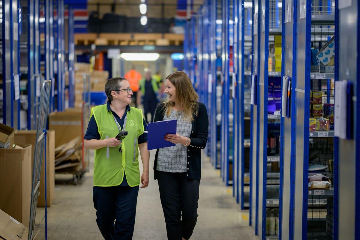 Two colleagues walking a warehouse aisle with a stock-count sheet
