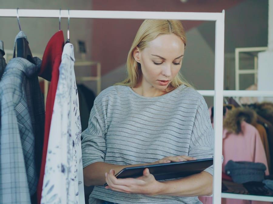 A retailer checking stock on a tablet beside a clothing rail